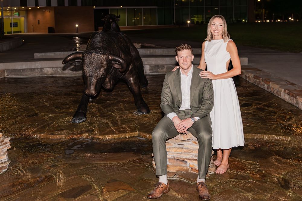 Couple posing at night in front of a bronze bull statue at a university campus.