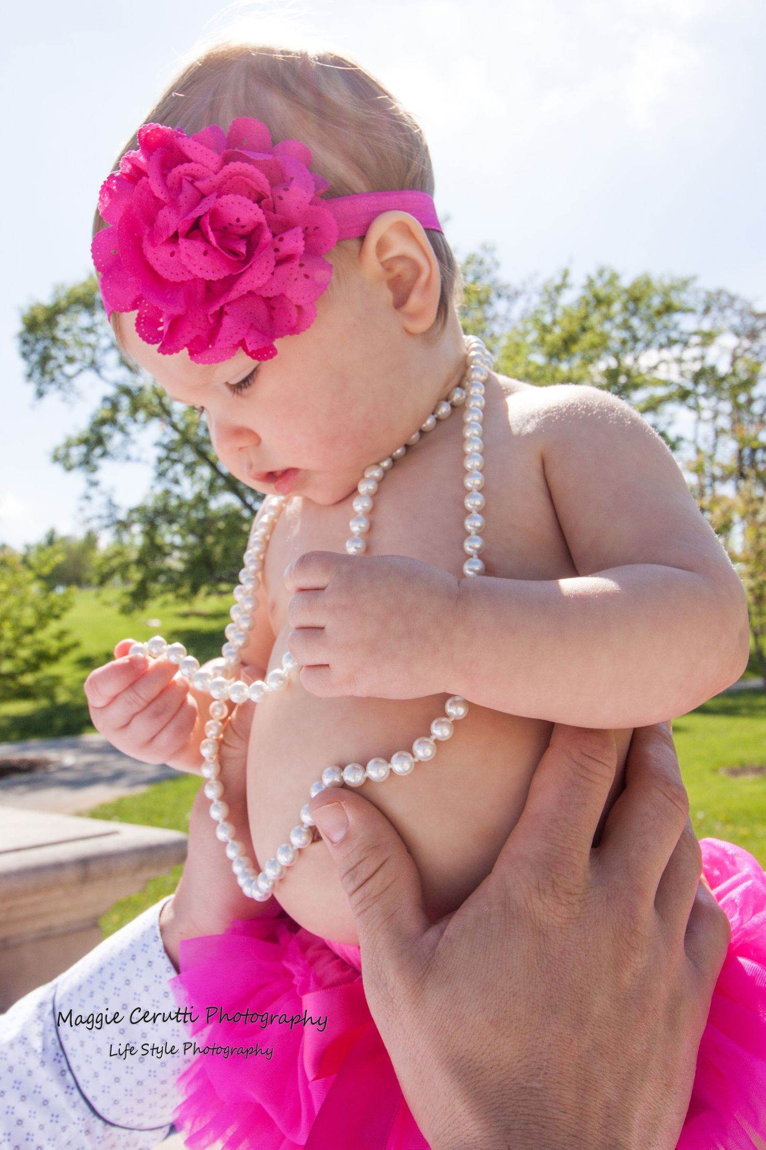 Family portrait of baby wearing a pink tutu, pink headband and a strink of pearls.