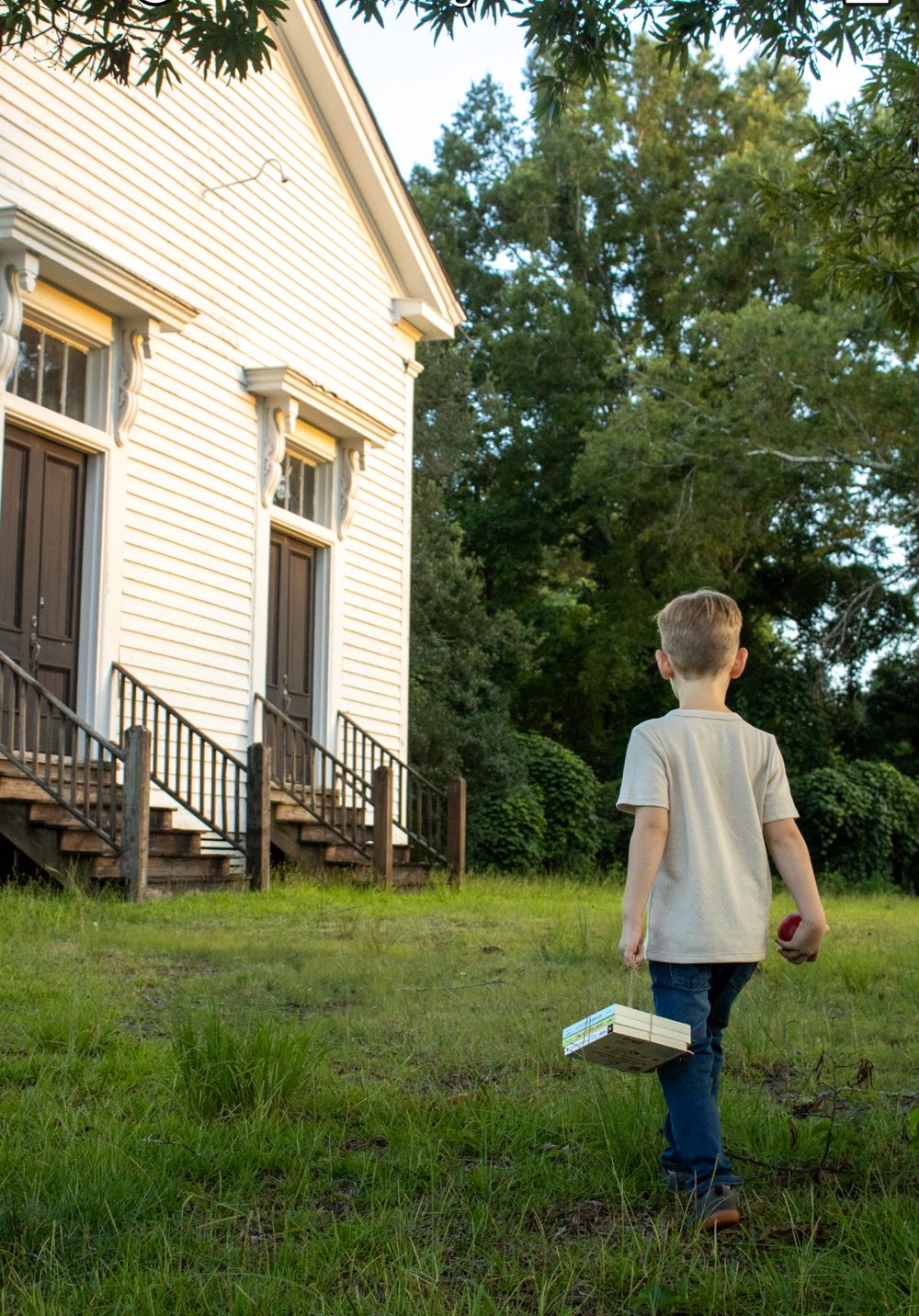 A child walks up a grassy hill towards a white house on a sunny day.