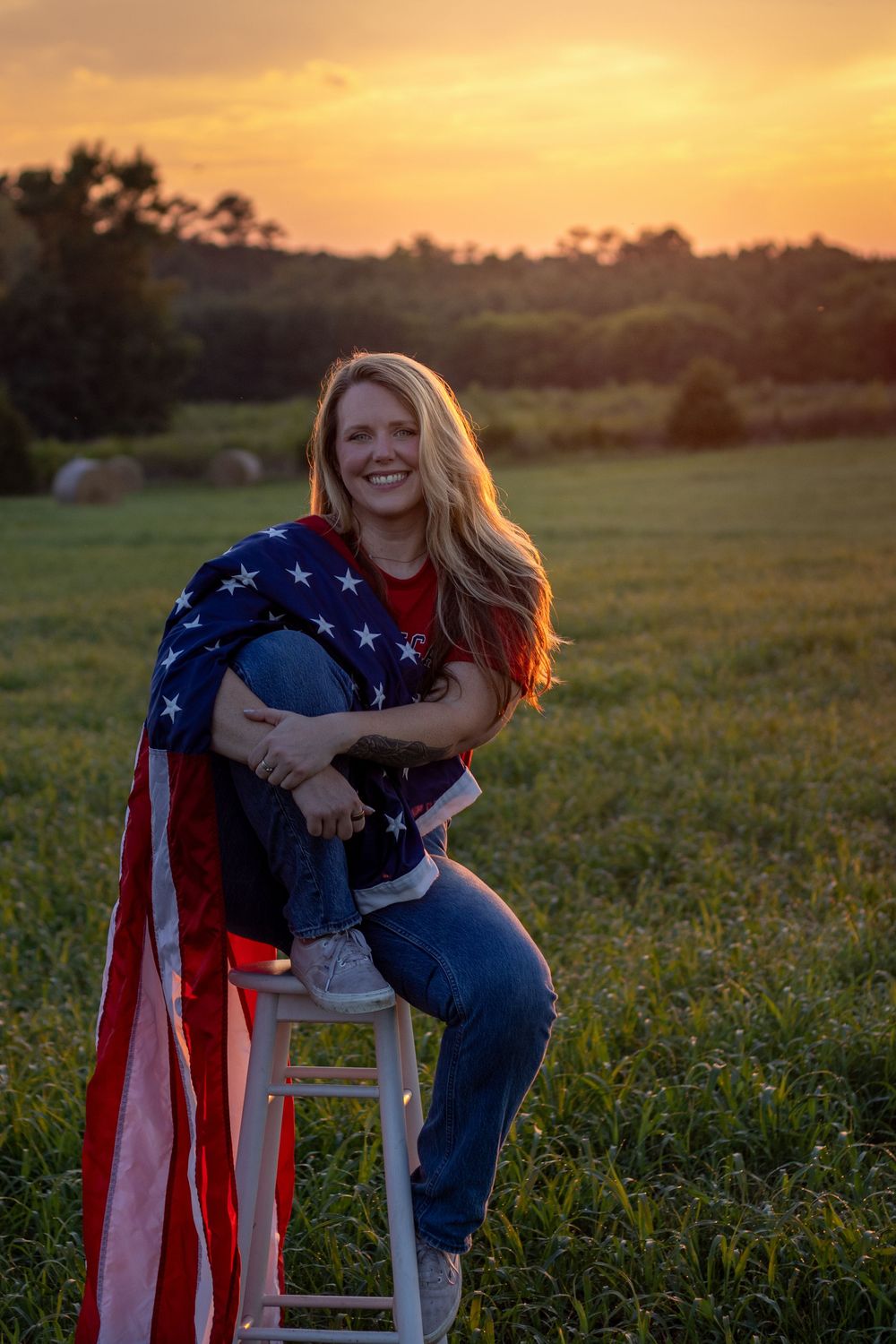 A patriotic portrait photoshoot in a green field during South Carolina sunset with American flag captured by Raley and Roots Photography.