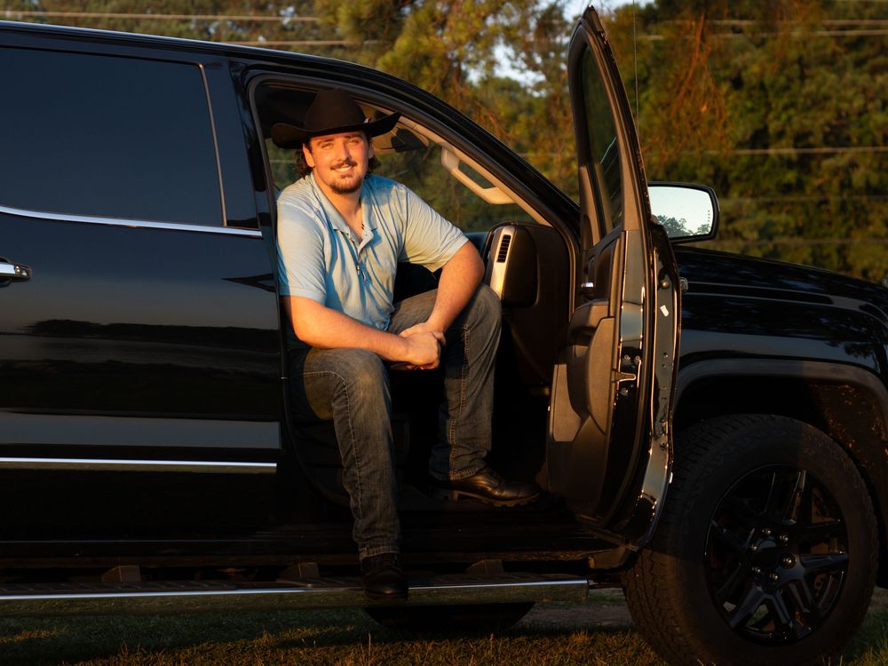 Man sitting in the doorway of his black truck at sunset during a portrait outdoor photo shoot captured by Raley and Roots Photography.