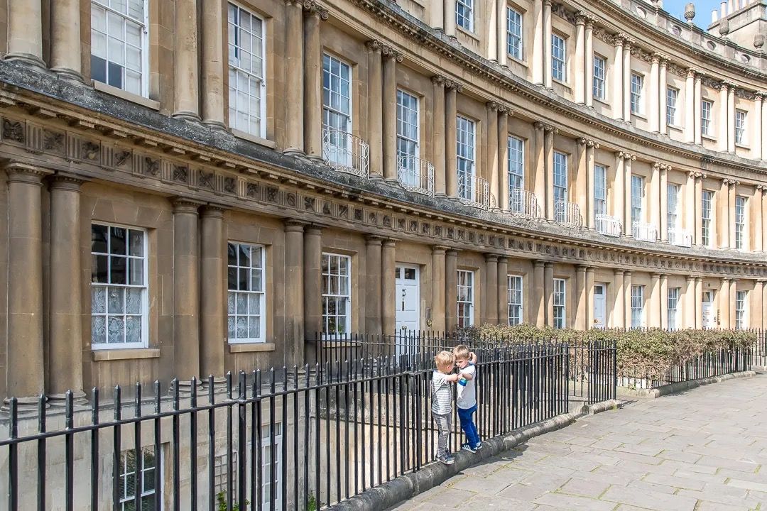 Curved Georgian terrace with stone columns, railings, and a children walking along the pavement.
