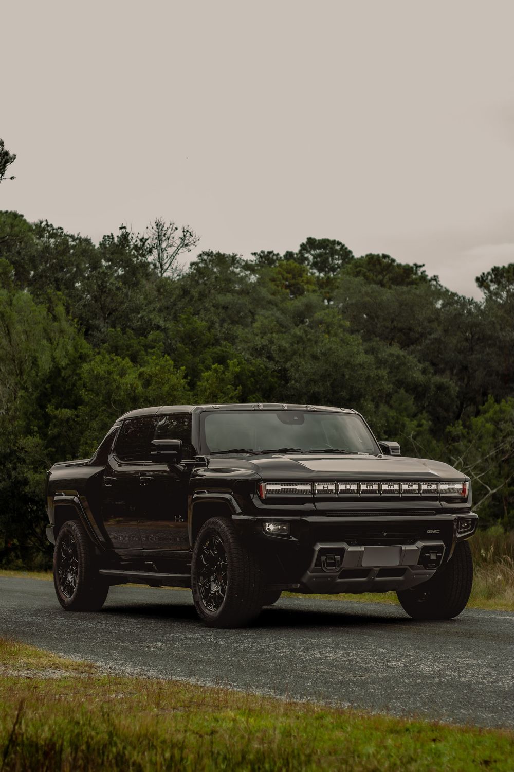 Black luxury sports car photographed from multiple angles on a rural road with trees in the background.