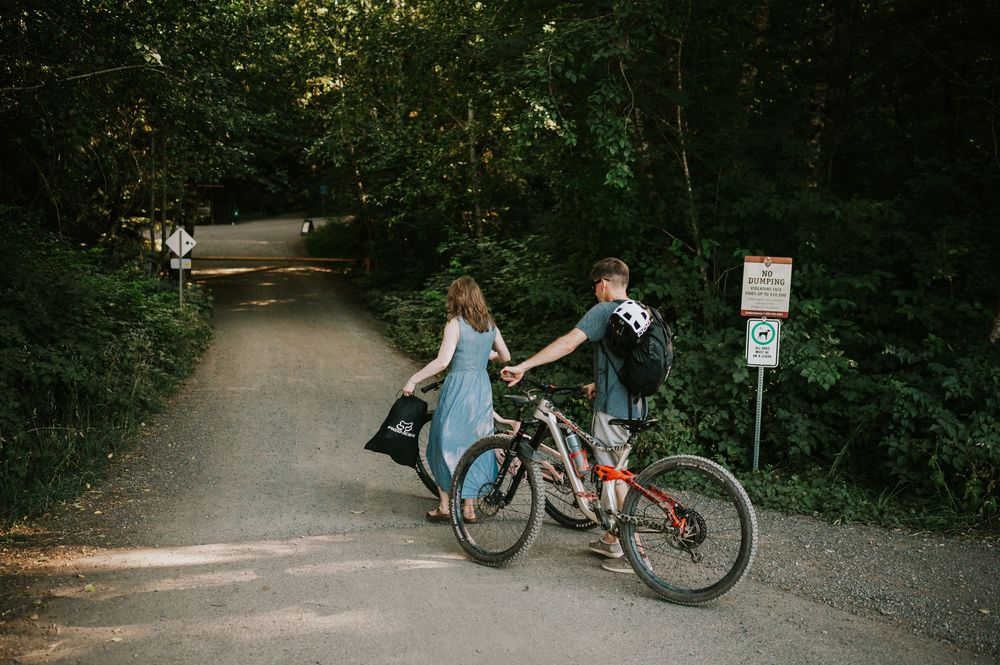 Adventurous couple photographer mountain biking into Cumberland Forest Vancouver Island engagement session walking bikes