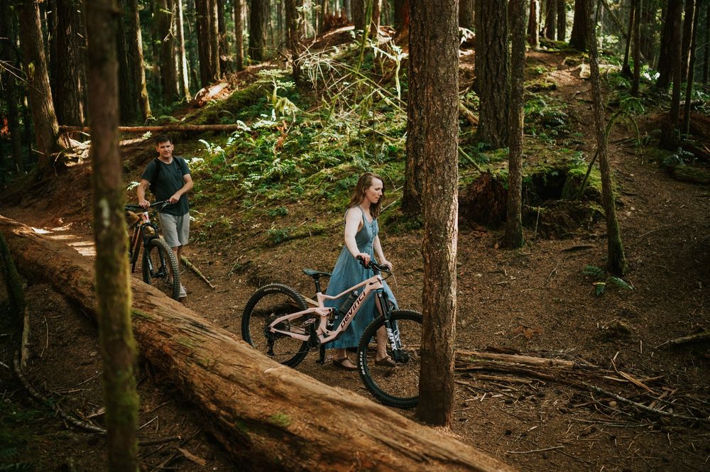 Adventurous couple engagement session photographer photoshoot of couple Cumberland Forest Vancouver Island walking mountain bikes on trail