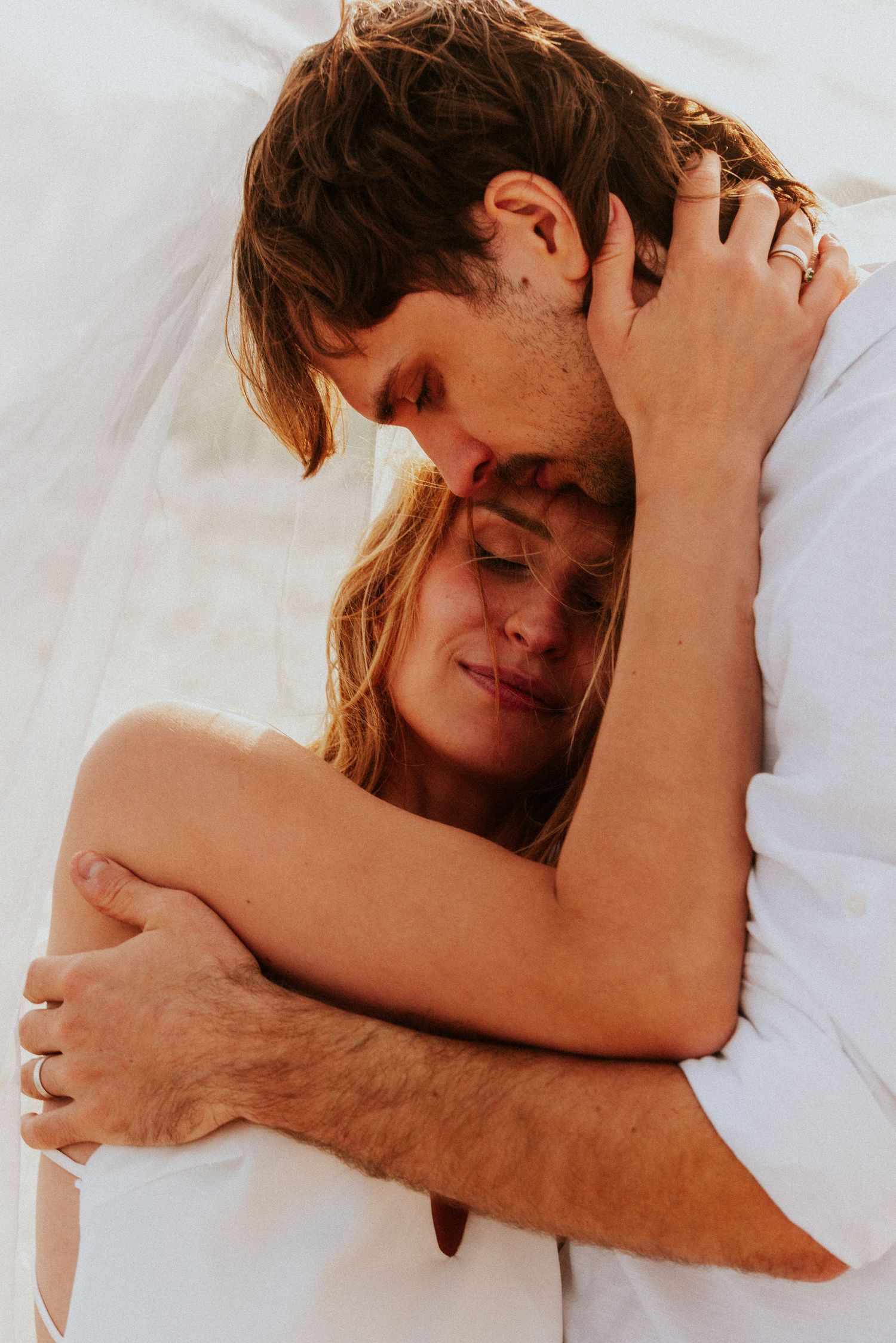 Intimate series of romantic couple embracing and cuddling in bed with white sheets.