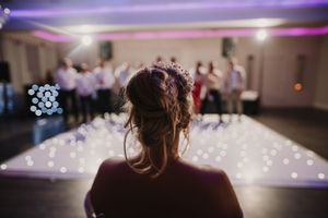 Wedding reception dance floor illuminated with purple and pink lighting and string lights creating a romantic atmosphere.