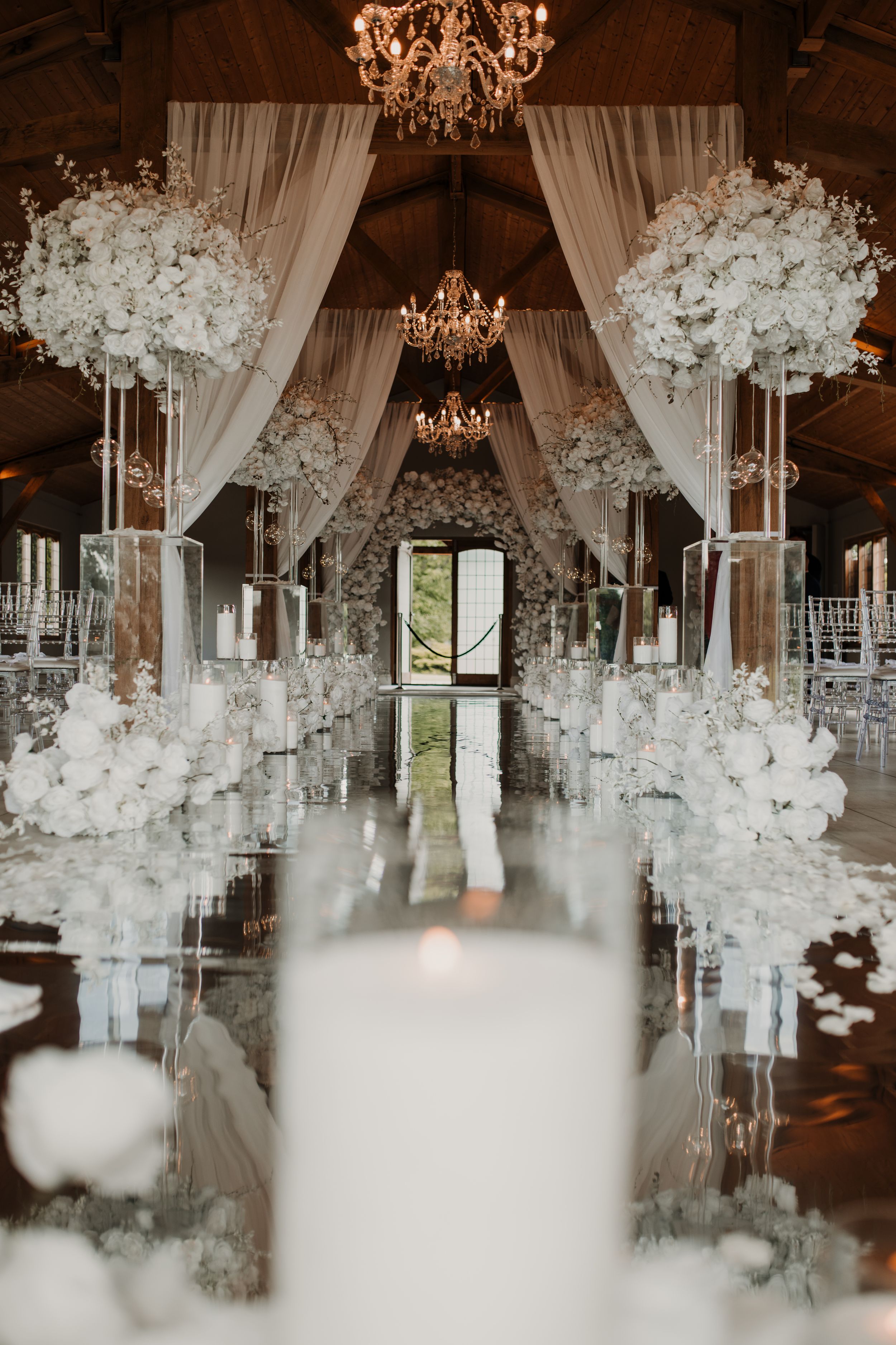 Elegant wedding reception decor with white floral arrangements, sheer drapes, and crystal chandeliers in a rustic venue at Merrydale Manor