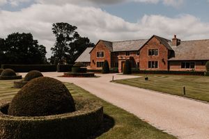 Rustic brick buildings and winding driveway on a scenic countryside property under cloudy skies at Merrydale Manor