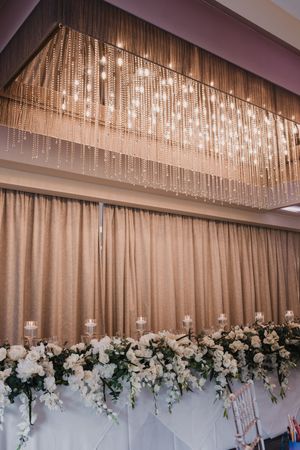 Elegant crystal chandelier installation above white floral arrangements at a wedding reception at Merrydale Manor