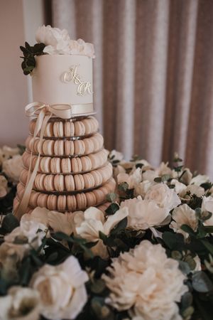 Tiered display of blush pink macarons surrounded by white roses and greenery for a wedding dessert table.