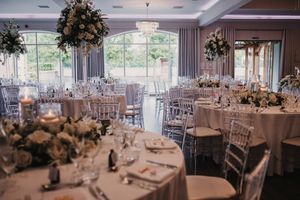 Elegant wedding reception venue with white chairs and floral centerpieces arranged in rows under crystal chandeliers.