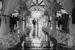Elegant black and white wedding ceremony setup with draped fabric, floral arrangements, and chandelier lighting.