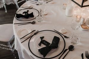 Elegant table setting with black and white plates, silverware, and wine glasses on crisp white tablecloth.