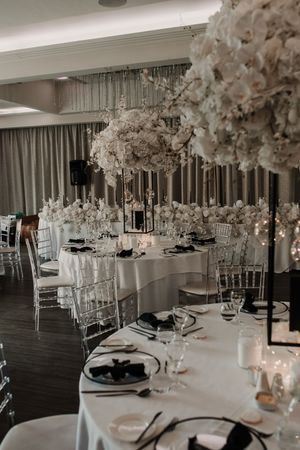 Elegant wedding reception tables with white floral centerpieces, crystal glassware, and dark wood flooring in a modern venue.