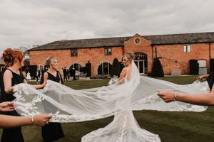 A flowing white wedding veil billows dramatically in the wind against a backdrop of rustic brick buildings at Merrydale Manor
