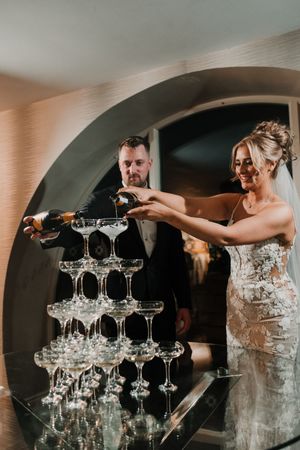 People pour champagne into a tower of crystal glasses during an elegant wedding celebration at Merrydale Manor