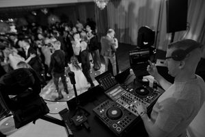 DJ performing at a nightclub with professional mixing equipment and turntables while a crowd dances in the background.