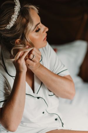 A person putting on earrings while wearing a white button-up top and crystal hair accessory.