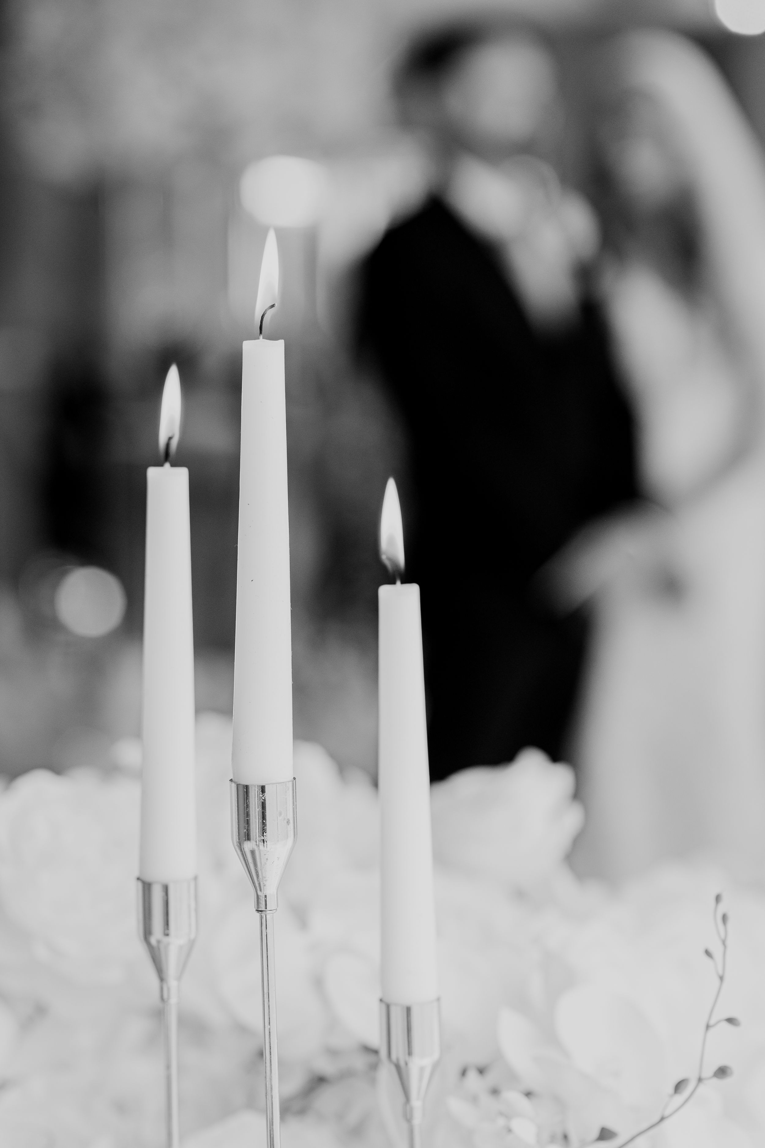 Three lit white candles in silver holders create an elegant ambiance with a soft blurred background at Merrydale Manor