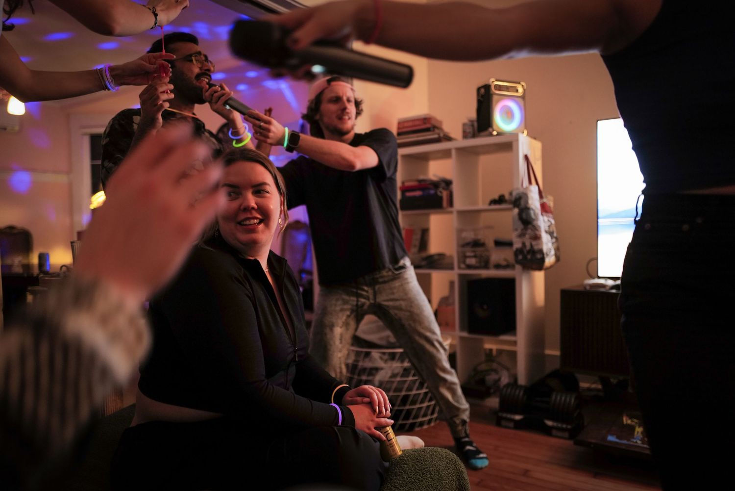 Friends laugh and dance during a lively indoor house party with colorful lighting.