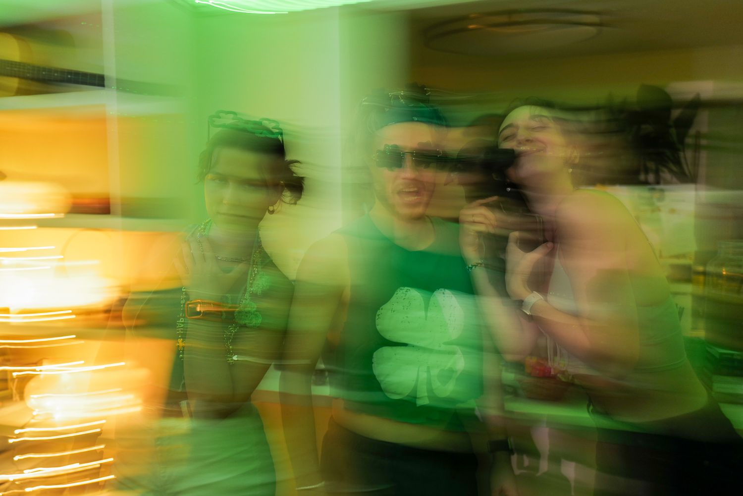 Blurry motion photo of a group of friends in a green-lit room celebrating St. Patrick's Day.