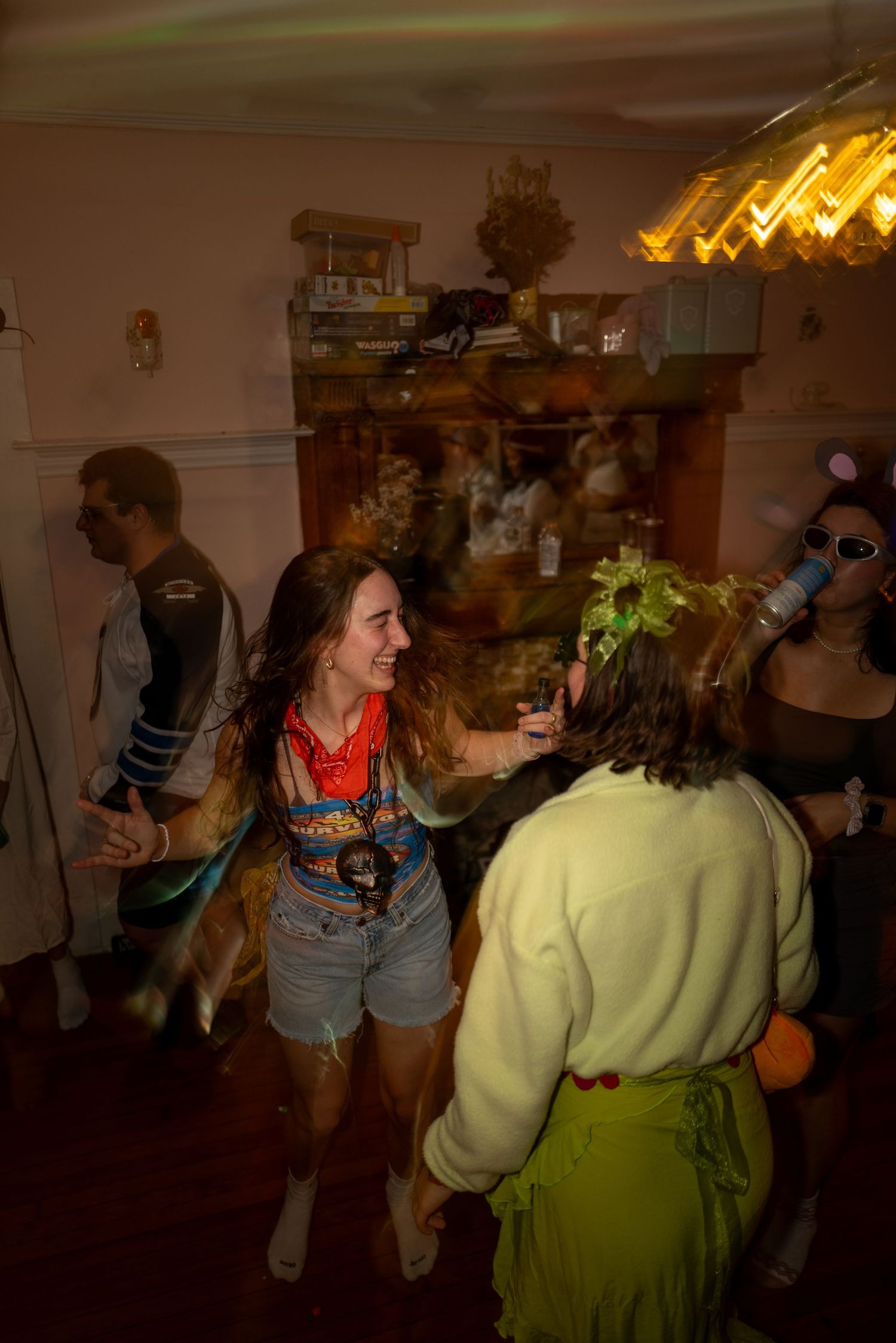 Two women dancing and laughing together at a lively indoor house party with warm lighting.
