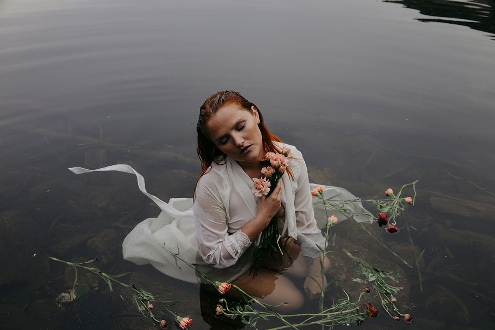 Artistic underwater portrait with floating flowers and flowing white fabric in dark waters.