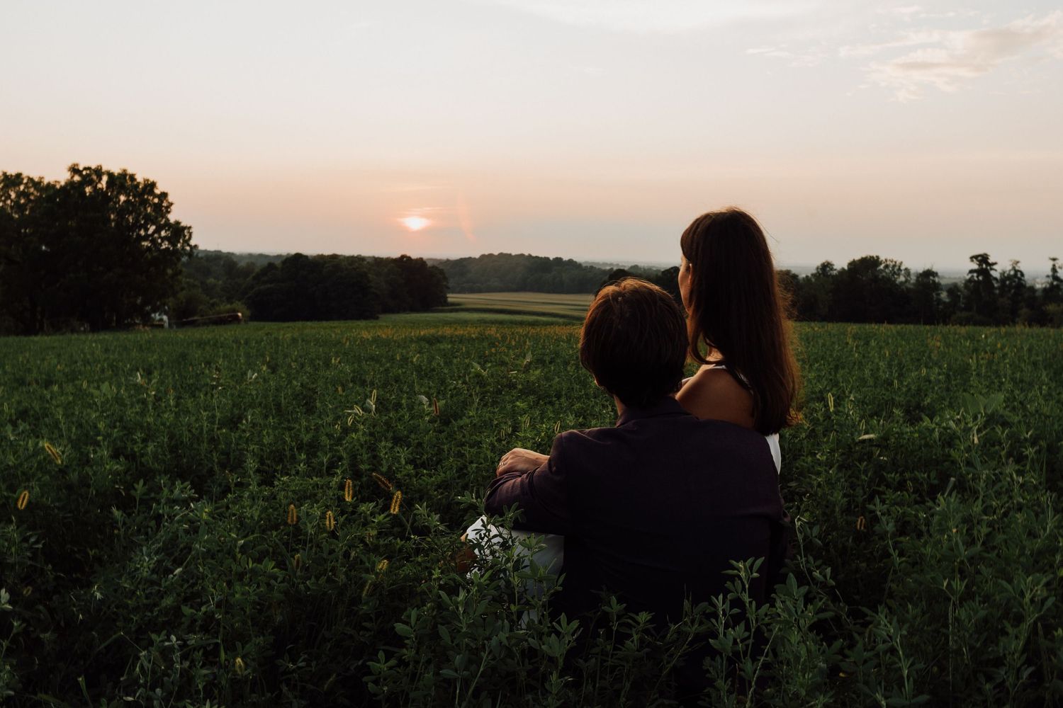 A scenic view of green agricultural fields at sunset with bride and groom posing looking at sunset at Wildflower Lookout in Ronks, PA.