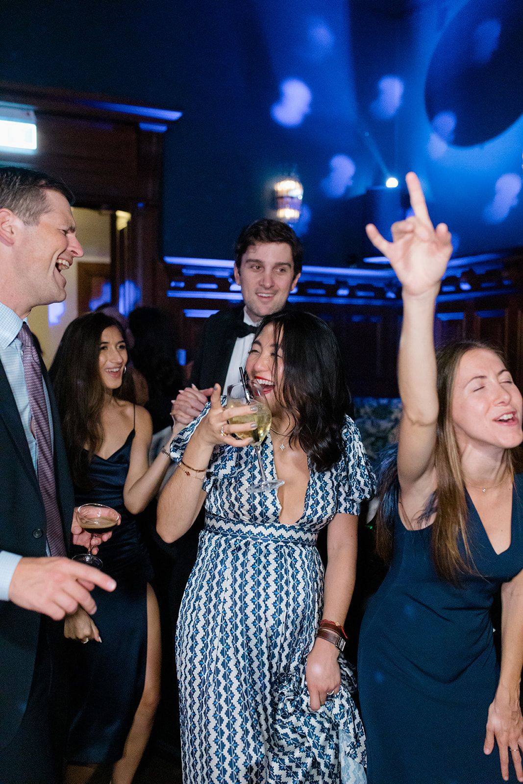 Party guests dance and celebrate on a dimly lit dance floor with blue lighting and bokeh effects in the background.