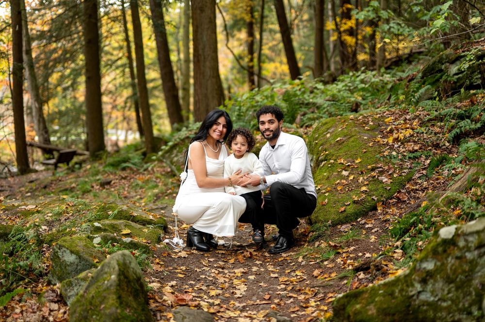 Family of three posing together on leaf-covered path in autumn forest.
