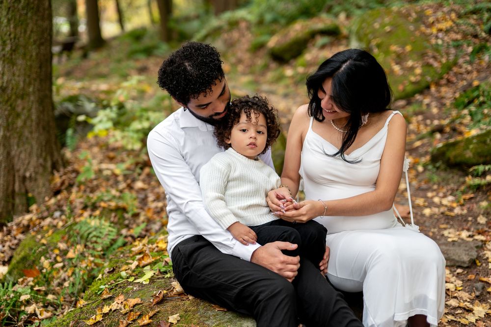 Young family of three sitting on rocks in autumn woodland examining something small together.