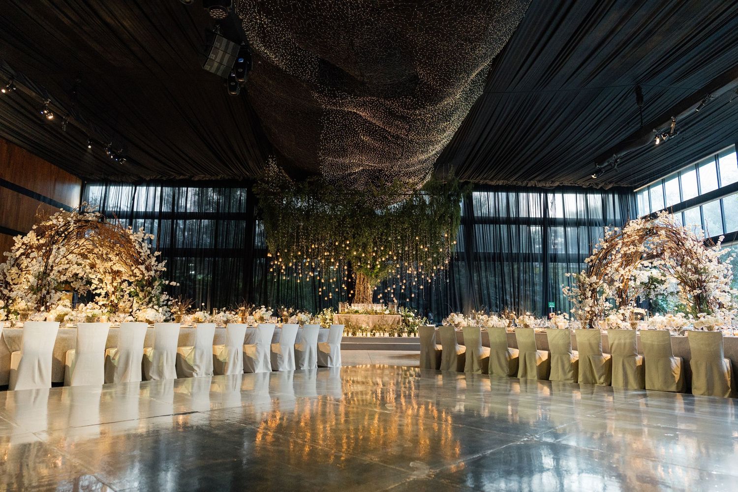 Panoramic view of an elegant wedding reception venue with white chairs and floral decor under dramatic lighting.