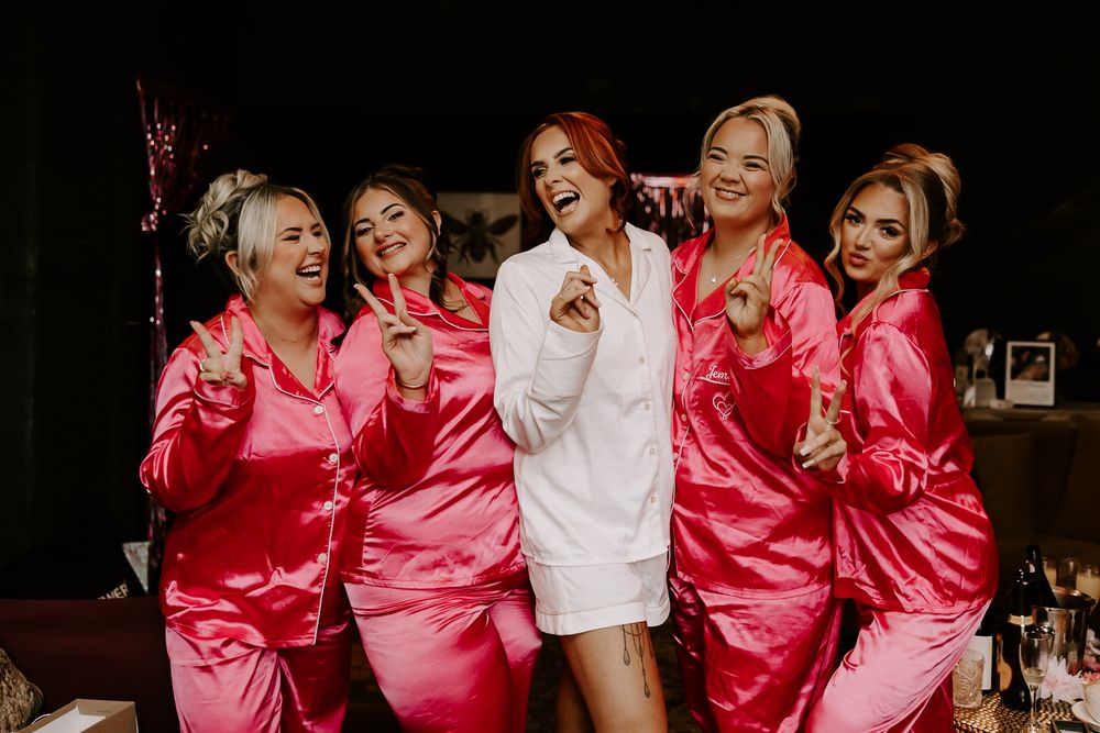 Group wearing pink and white satin robes laugh and pose together during a celebration event.