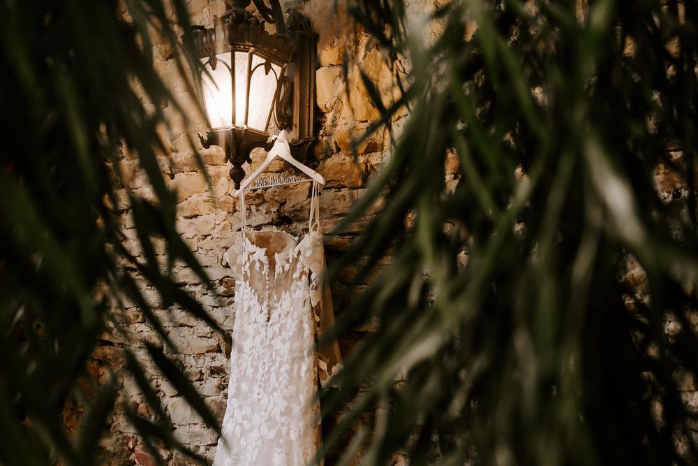 A rustic chandelier with delicate crystal details hangs from a wooden beam in an elegant barn setting.