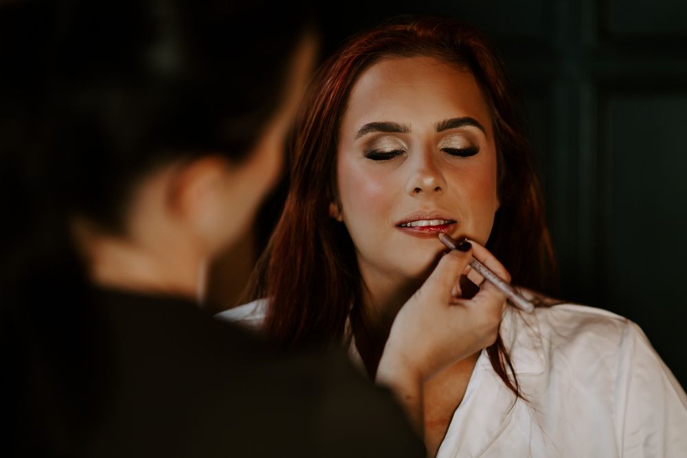 Professional makeup artist applies finishing touches to a bridal look in a dark moody setting.