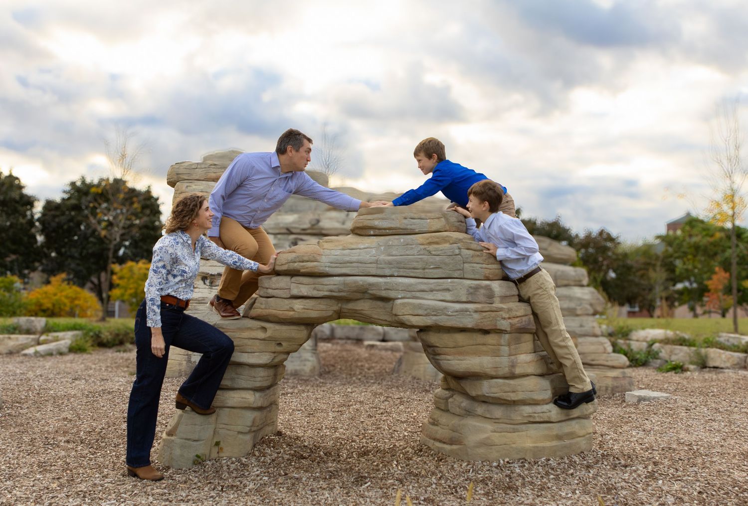 Two children play on a natural stone arch structure in a park setting.