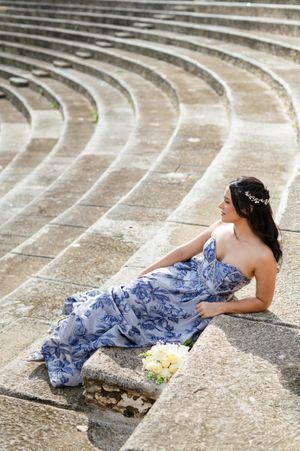A person in a blue floral gown reclines on stone amphitheater steps with a white bouquet nearby.