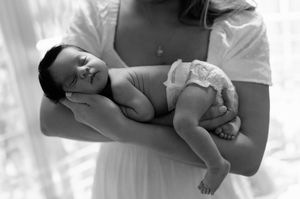 Black and white photo of a baby being held and cradled in someone's arms.