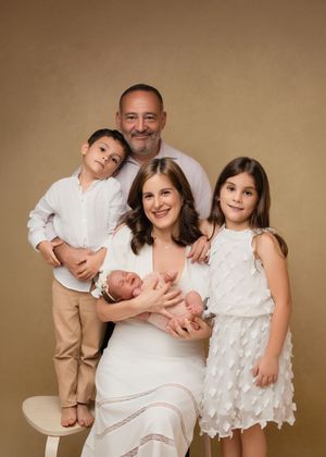 Family portrait in neutral tones with a newborn baby and three older family members wearing coordinated white outfits.
