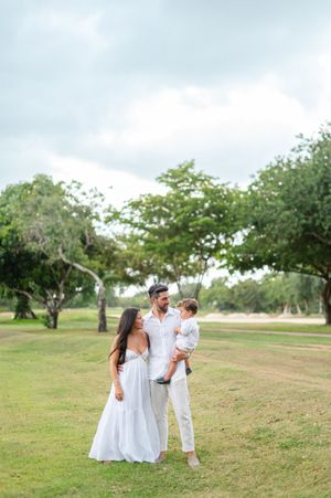 Family wearing white outfits poses together on grassy hill during outdoor photo session.