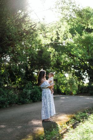 Sunlit garden path with figures in matching floral dresses standing together in a natural outdoor setting.
