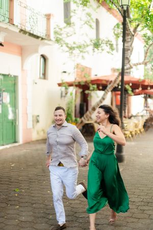 Couple enjoying a playful moment together on a charming cobblestone street lined with pastel buildings.
