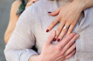Close-up of hands with burgundy nail polish and engagement ring on white linen fabric.