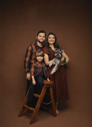 A family poses with their pet rabbit on a wooden chair against a dark brown studio backdrop.