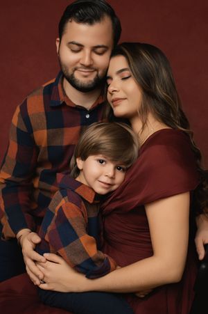 A family poses together in burgundy and navy plaid outfits against a dark maroon backdrop for professional portraits.