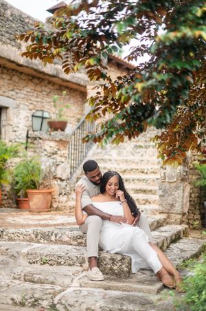 Romantic couple embraces on rustic stone steps of Mediterranean villa surrounded by autumn foliage.