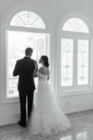 A black and white wedding photo series showing a couple walking down a bright hallway with arched windows.
