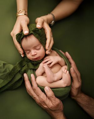 A series of artistic photos showing gentle hands cradling a sleeping newborn baby against a dark green background.