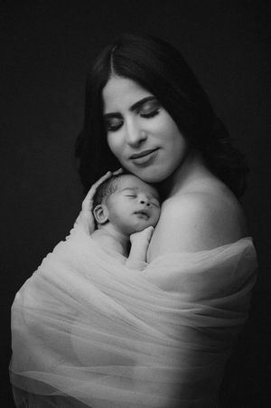 Black and white artistic portrait series showing tender moments between mother and sleeping newborn baby in soft lighting.